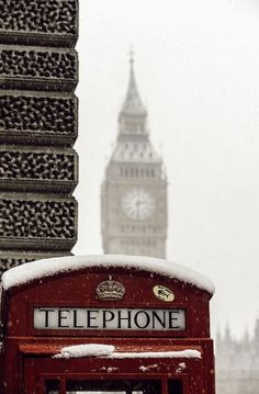 a red phone booth in the snow with big ben in the background on a snowy day