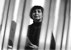 black and white photograph of an older woman looking out from behind the curtain in front of her