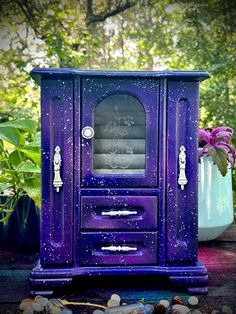 a purple cabinet sitting on top of a wooden table next to flowers and plants in vases