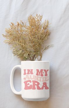 a coffee mug with the words in my favorite era printed on it and some dried plants