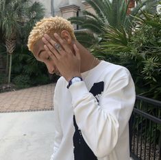 a young man covers his face with his hands as he stands in front of some palm trees