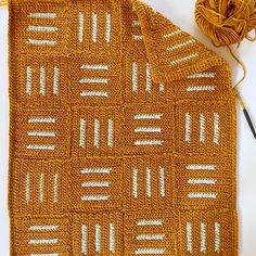 an orange crocheted blanket next to a ball of yarn and a knitting needle