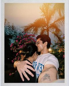 a man and woman embracing each other in front of some flowers with the sun behind them