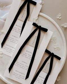 two black ties are tied to the back of some white wedding programs on a plate