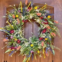 a wreath is hanging on the front door with flowers and greenery around it's edges