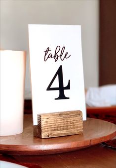 a table number sitting on top of a wooden plate next to a cup and candle