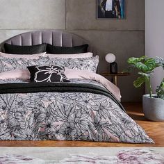 a bed with black and pink comforters in a bedroom next to a potted plant