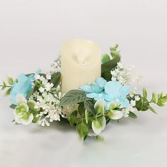 a white candle surrounded by blue flowers and greenery