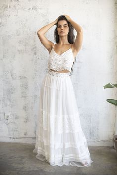 a woman standing in front of a wall wearing a white skirt and cropped top