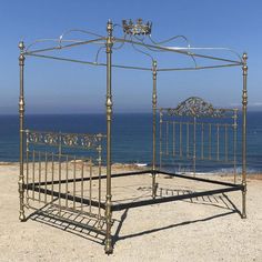 an iron bed frame on the beach with ocean in the backgrouds and blue sky