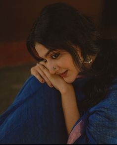 a woman sitting on the ground with her hand under her chin and looking at the camera