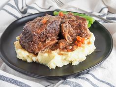 a black plate topped with meat and mashed potatoes covered in gravy next to green beans