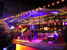 people are standing outside at night with lights on the roof and tables in front of them