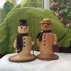 two wooden snowmen standing next to each other on a white tablecloth covered bed