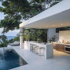 an outdoor kitchen next to a swimming pool and trees with the ocean in the background