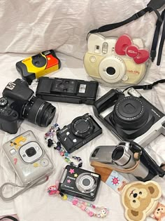 many different types of cameras are laying on a white sheet with teddy bears and other items