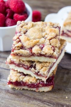 raspberry crumb bars stacked on top of each other next to a bowl of raspberries