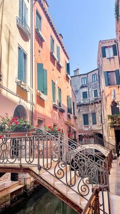 a bridge that has flowers growing on it and some buildings in the background with green shutters