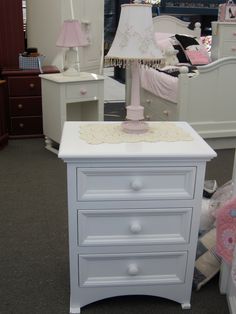 a white night stand with pink lamps on it in a room filled with other furniture