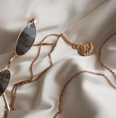 a pair of sunglasses laying on top of a white sheet with a gold chain around it