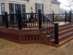 a wooden deck with black railing and handrails in front of a brick house