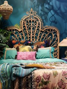 a bed with lots of colorful pillows and blankets on it's headboard in front of a blue wall