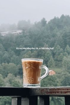 a cup of coffee sitting on top of a wooden table next to a forest filled with trees