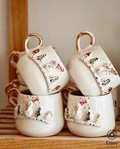 four white ceramic cups with gold handles and decorated christmas decorations on them, sitting on a shelf