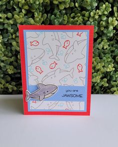 a card with an image of a whale and fish on it, in front of some green bushes