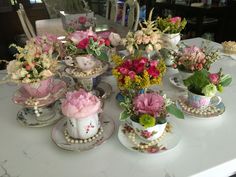 a table topped with tea cups and saucers filled with different types of flower arrangements