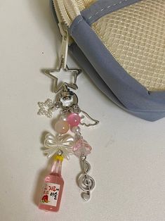 a pink bottle with charms hanging from it next to a blue purse on a white table