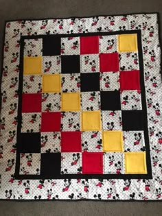 a mickey mouse quilt on the floor with red, yellow and black squares in it