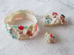 three bracelets and two figurines sitting on a white tablecloth covered surface