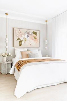 a white bed sitting under a painting on the wall