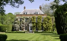 a large brick house surrounded by lush green trees and bushes in front of it is covered with wistery vines