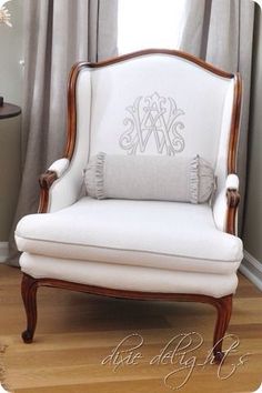 a white chair with a monogrammed pillow on it's back in front of a window