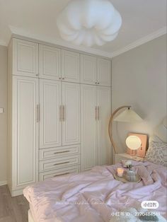 a bedroom with white closets and pink bedspread on the bed, next to a lamp