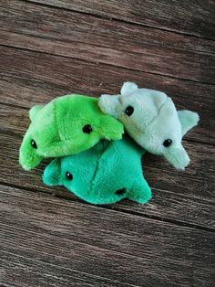 three stuffed animals laying on top of a wooden floor next to each other, one green and the other white