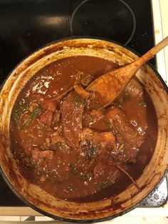 a pot filled with meat and vegetables cooking on top of a stove burner next to a wooden spoon