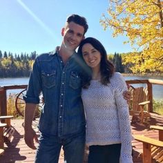 a man standing next to a woman on top of a wooden deck near a lake