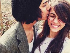 a man and woman kissing each other in front of a fence with trees behind them