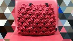 a red crocheted bag sitting on top of a pink chair with black handles