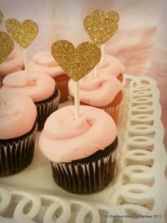 cupcakes with pink frosting and gold glitter hearts on top are sitting on a white plate