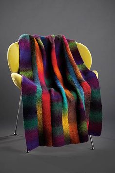 a multicolored blanket sitting on top of a chair next to a yellow chair