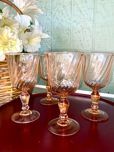 four wine glasses sitting on top of a table next to a basket with flowers in it