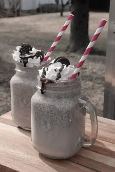 two mason jars filled with ice cream and toppings on a wooden table outside in the sun