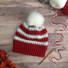 a red and white knitted hat next to yarn, crochet needles and flowers