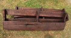 an old wooden box sitting on the ground with grass in front of it and one piece missing