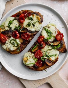 two slices of toast with tomatoes, mozzarella and basil on them sitting on a white plate