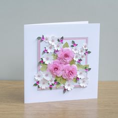 a card with pink roses and white flowers on the front, sitting on a table